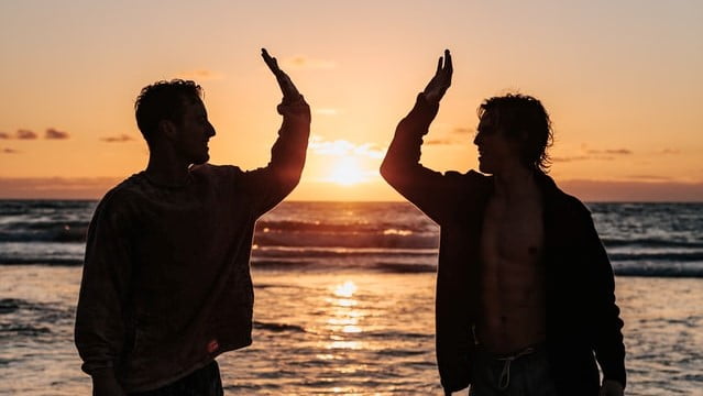 Zwei Personen am Strand klatschen sich ab (high five) um den Erfolg von frühzeitigem Anlegen zu feiern.