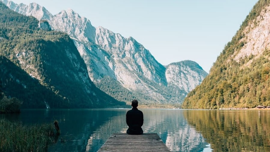 Une personne est assise sur un ponton avec vue sur un lac de montagne. Elle sait qu'investir des sommes importantes avec findependent fonctionne à merveille.