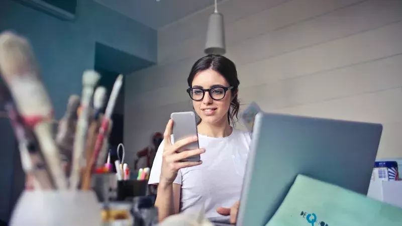 Digitale Vermögensverwalter Schweiz - findependent - Frau die ein Smartphone in der Hand hält, lächelt und vor einem Laptop sitzt